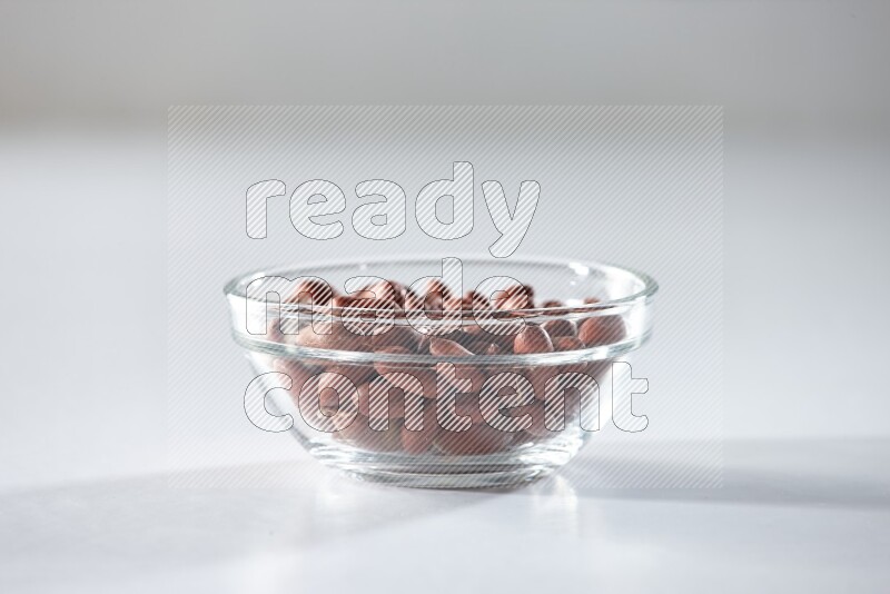 A glass bowl full of red skin peanuts on a white background in different angles