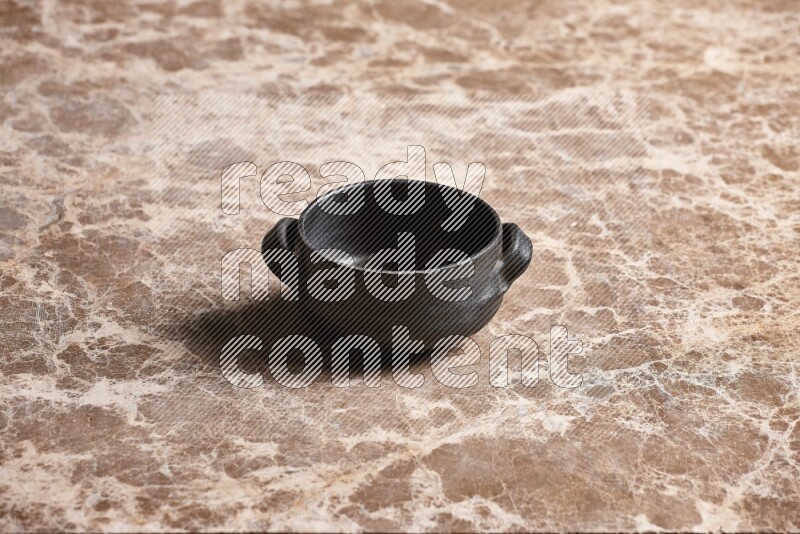 A black pottery bowl on beige marble background