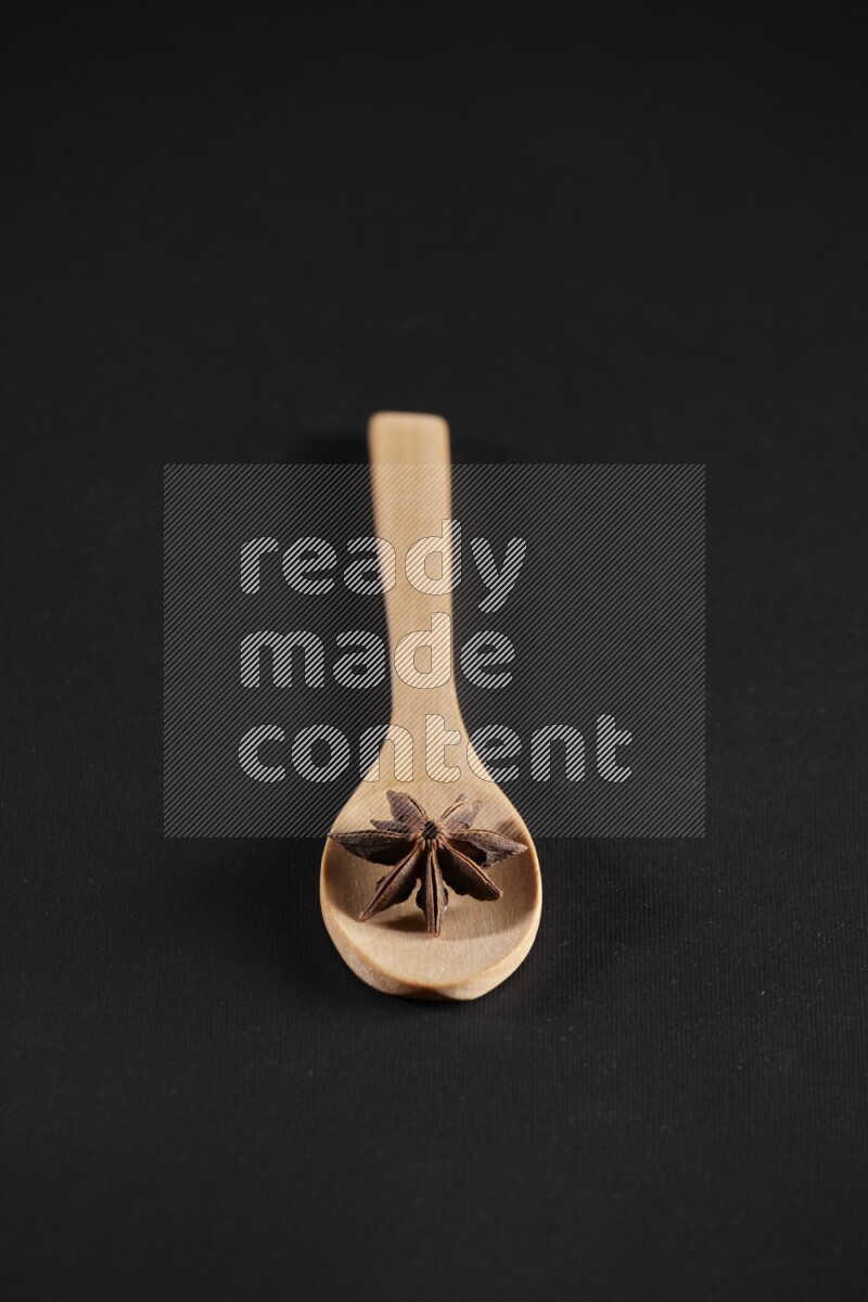 اليانسون النجمي في ملعقة خشبية فوق اليانسون النجمي الذي يغطي الإطار على أرضية سوداء