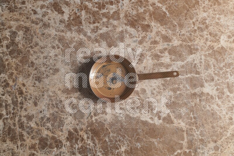A small copper pan on beige marble background