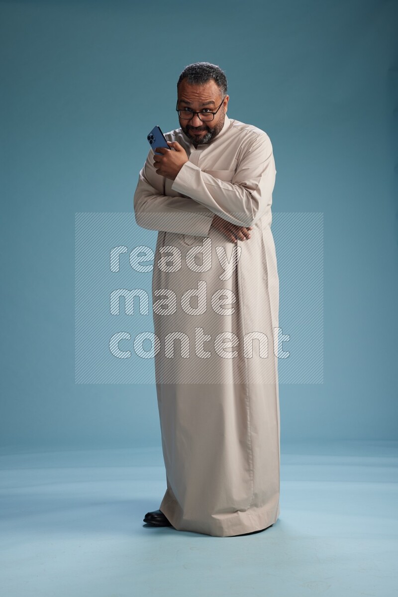 Saudi Man without shimag Standing texting on phone on blue background