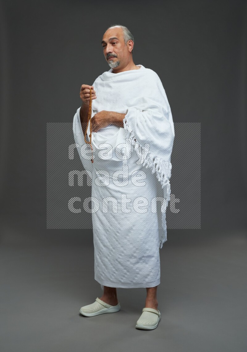 A man wearing Ehram Standing holding rosary on gray background
