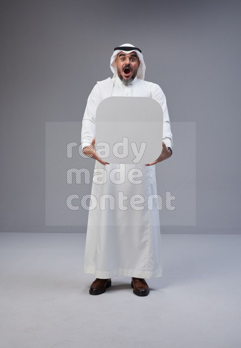 Saudi man Wearing Thob and white Shomag standing holding social media sign on Gray background