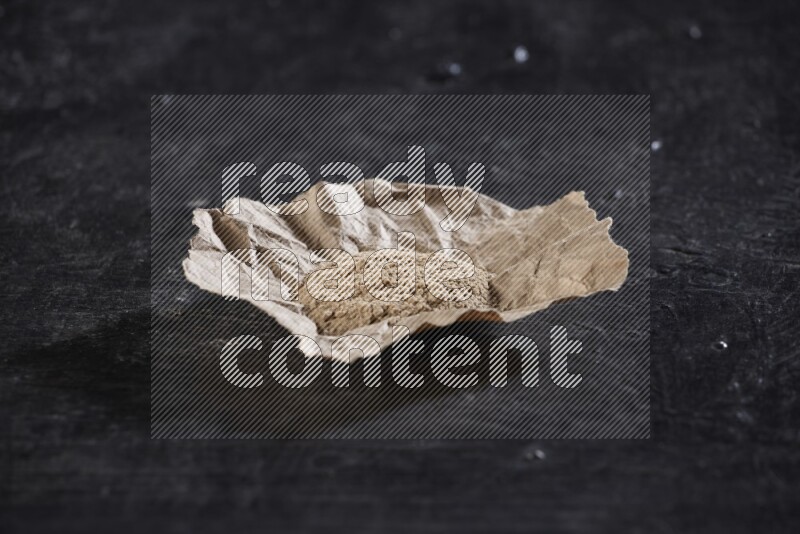 A crumpled piece of paper full of garlic powder placed on a textured black flooring