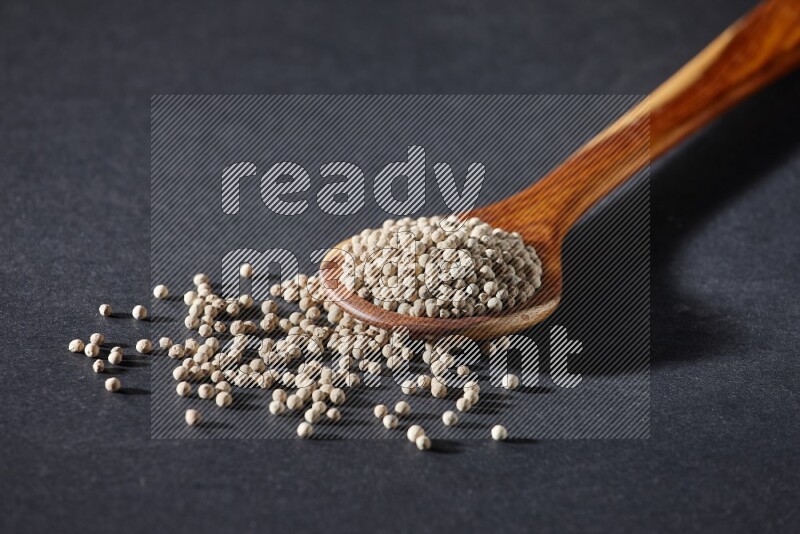 A wooden ladle full of white pepper beads on black flooring