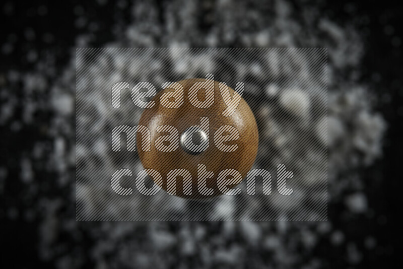 A wooden grinder standing upright and surrounded by coarse white sea salt on black background