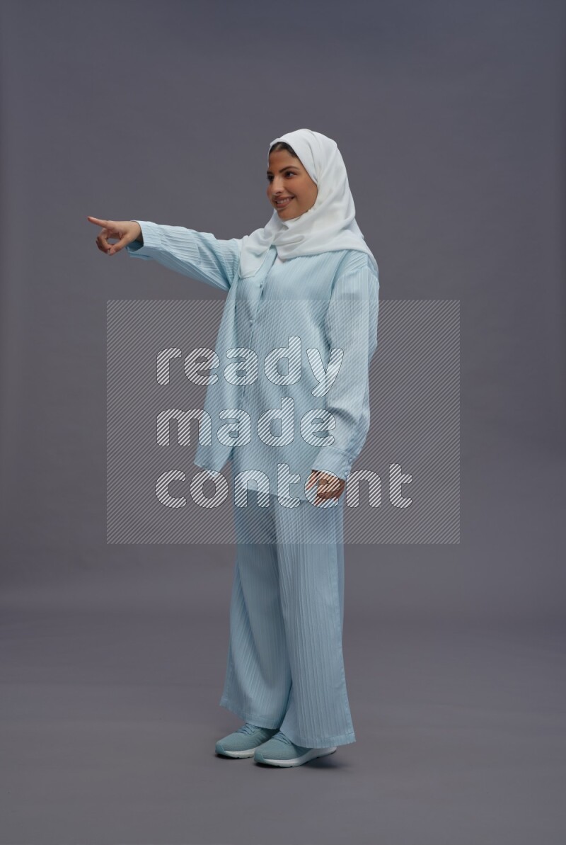 Saudi woman wearing hijab clothes standing interacting with the camera on gray background