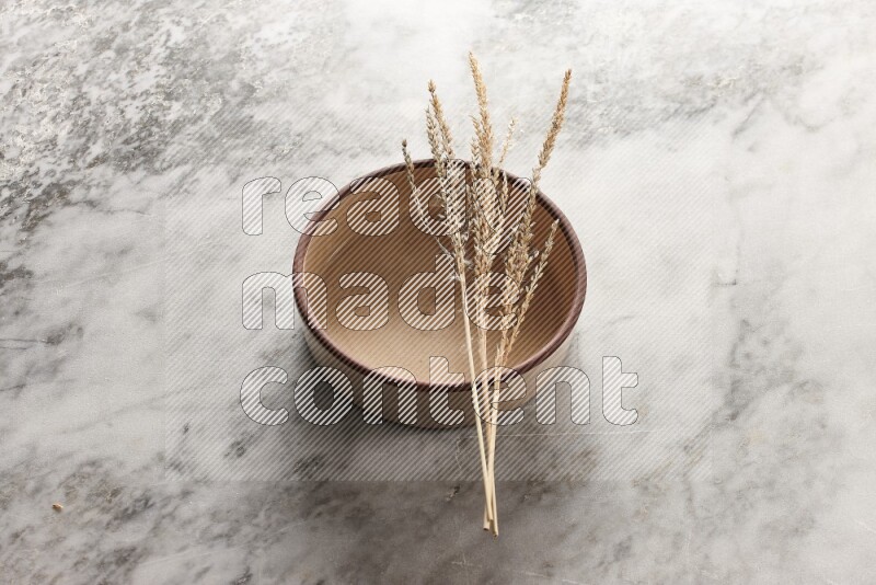 Wheat stalks on beige pottery oven bowl on grey marble background