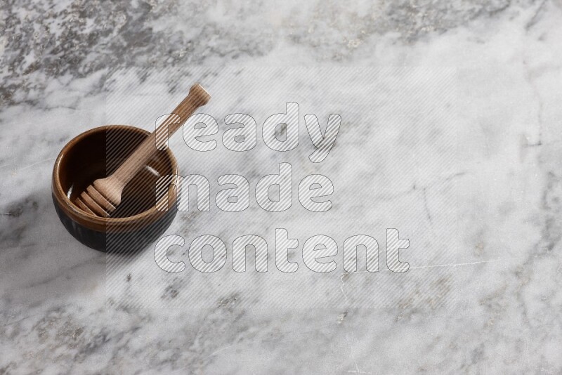 Multicolored pottery bowl with wooden honey dipper in it on grey marble background