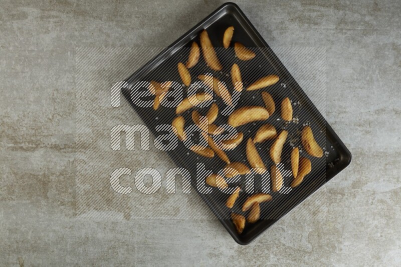 wedges potato in a black stainless steel rectangle tray on grey textured counter top