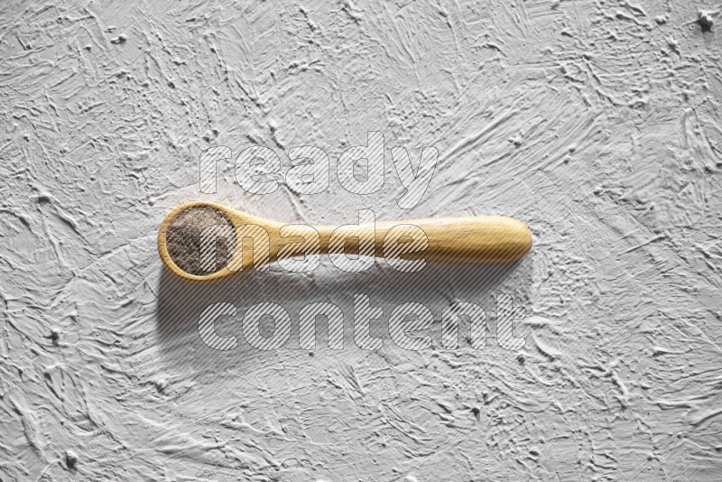 A wooden spoon full of black pepper powder on a textured white flooring