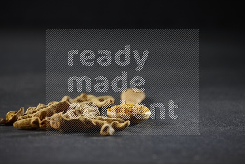 A wooden spoon full of turmeric powder with dried turmeric fingers on black flooring