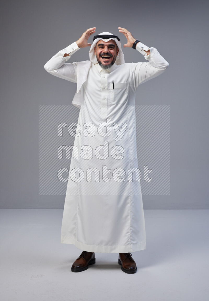 Saudi man Wearing Thob and white Shomag standing interacting with the camera on Gray background