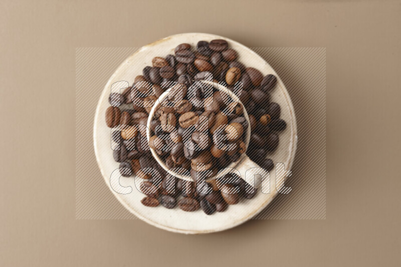 A beige pottery cup full of roasted coffee beans on beige background