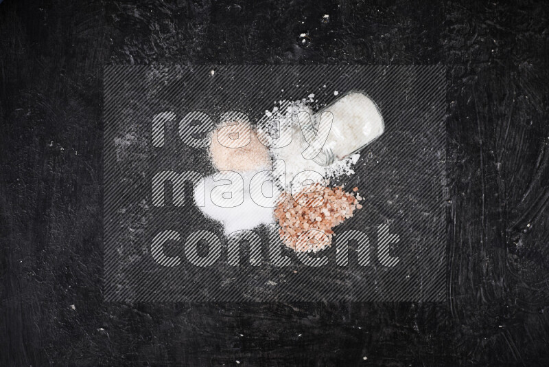 4 glass jars filled with table salt, coarse sea salt, fine himalayan salt and coarse himalayan salt on black background
