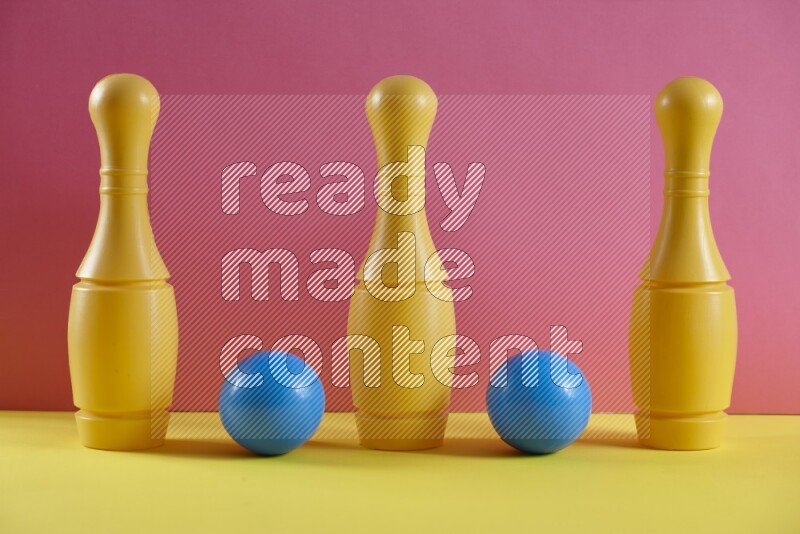 Plastic bowling pins with balls on pink and yellow background (kids toys)