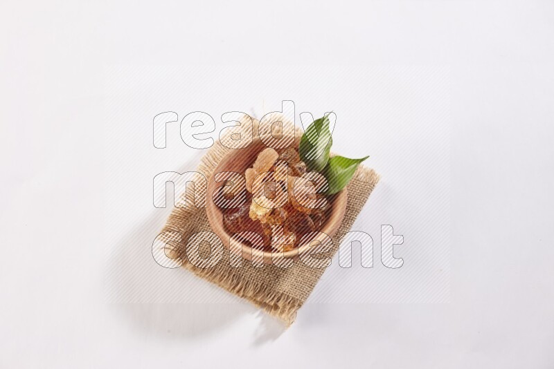 A wooden bowl full of gum arabic on a piece of burlap on white flooring