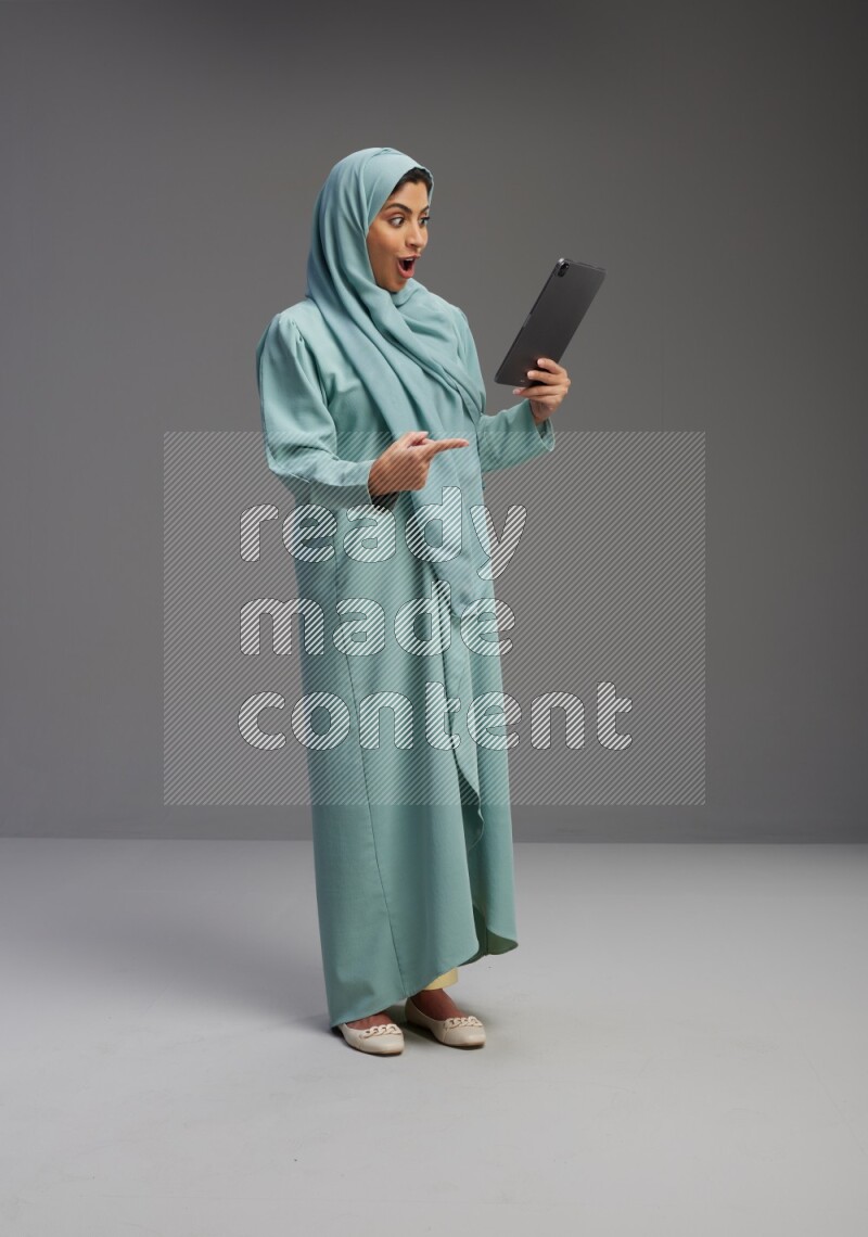 Saudi Woman wearing Abaya standing working on tablet on Gray background