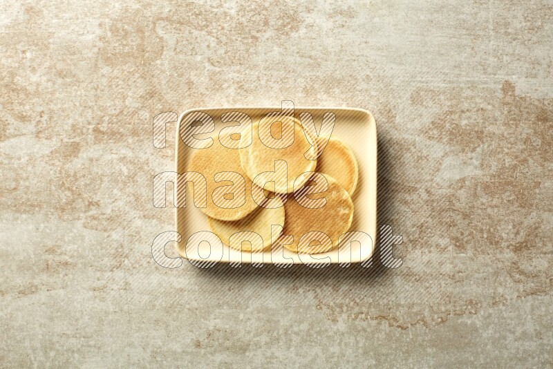 Five stacked plain mini pancakes in a rectangular plate on beige background