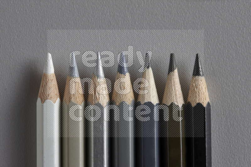 A collection of colored pencils arranged showcasing a gradient of white, grey and black hues on grey background