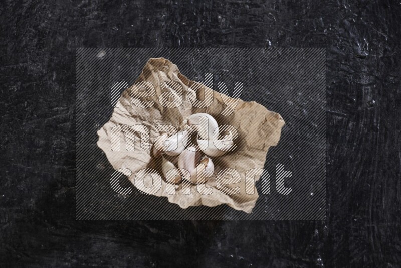 A crumpled piece of paper full of garlic cloves placed on a textured black flooring