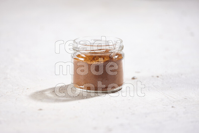 A glass jar full of ground paprika powder on white background