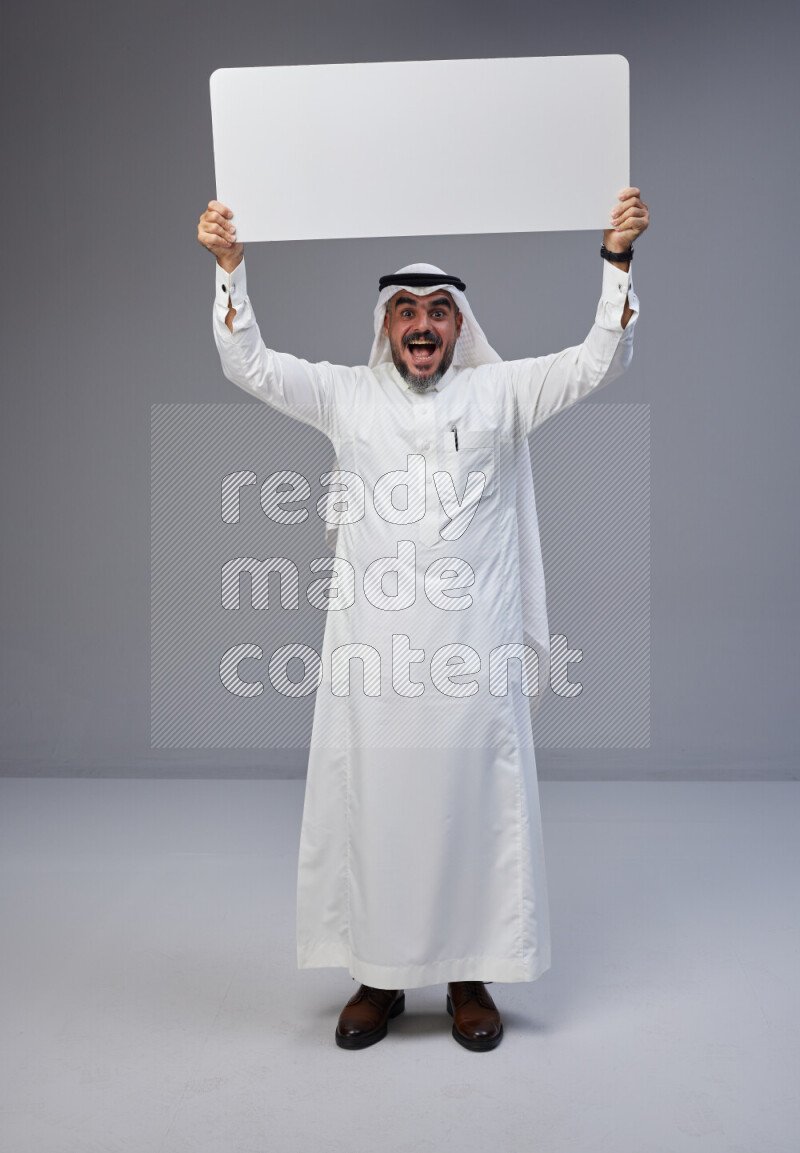Saudi man Wearing Thob and white Shomag standing holding board on Gray background
