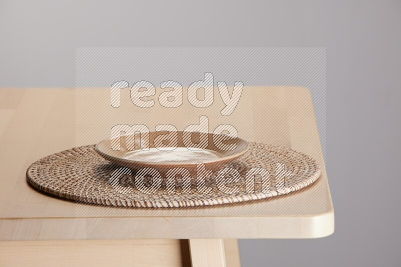 multi-colored pottery Plate placed on a big light colored straw placemat on the edge of wooden table