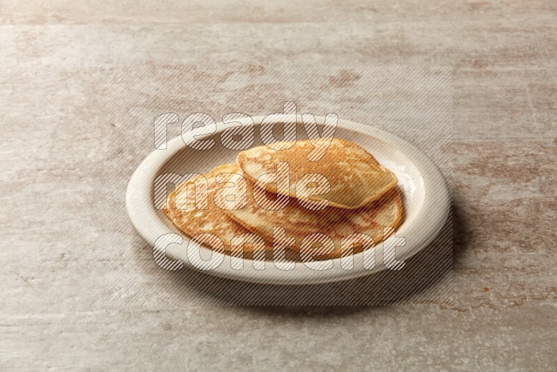 Three stacked plain pancakes in a beige plate on grey beige background