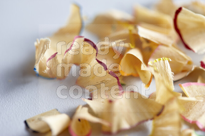 A close-up showing a small pile of pencil shavings with varied color edges on grey background