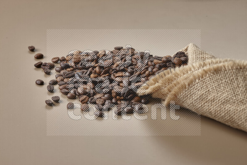 Spilled roasted coffee beans from its pack on beige background