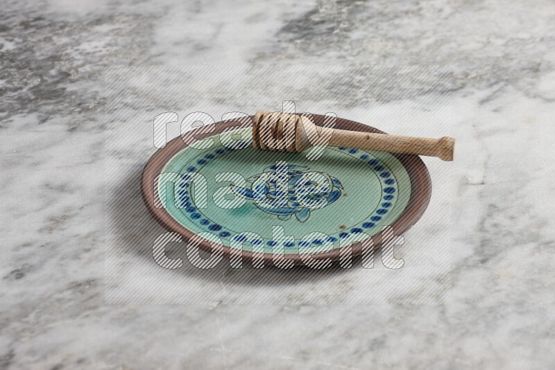 Decorative pottery plate with wooden honey dipper in it on grey marble background