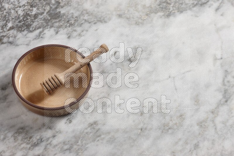 Beige Pottery oven bowl with wooden honey handle on the side with grey marble flooring, 65 degree angle