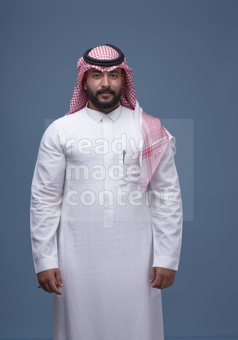 A man pointing on blue background wearing Saudi Thob with Shomag