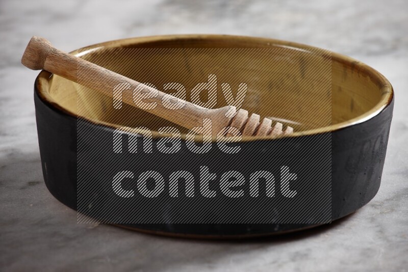 وعاء فرن فخاري متعدد الألوان مع ملعقة عسل خشبية بداخله على خلفية من الرخام الرمادي