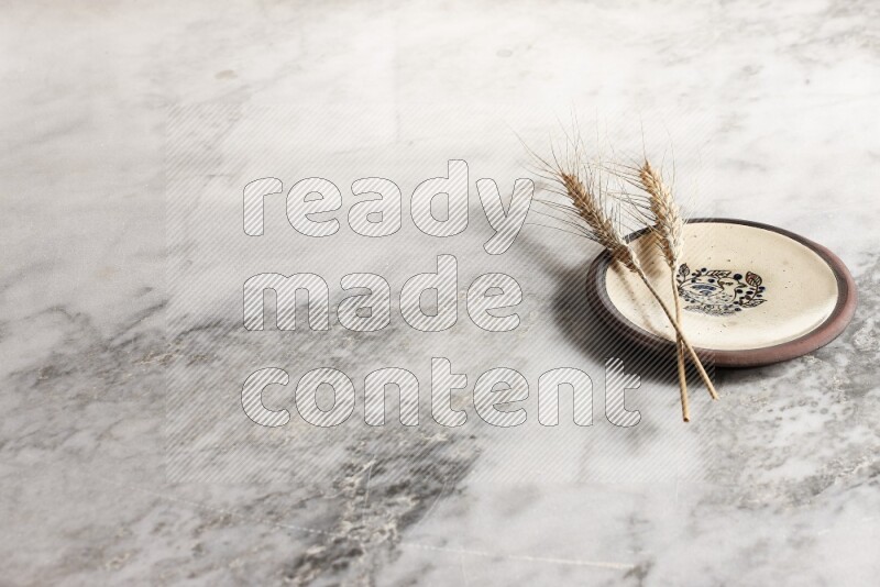 Wheat stalks on decorative pottery plate on grey marble background