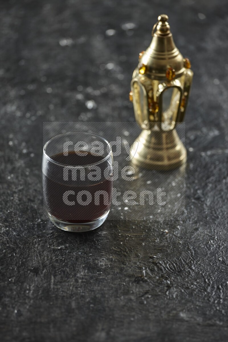 A golden lantern with different drinks, dates, nuts, prayer beads and quran on textured black background