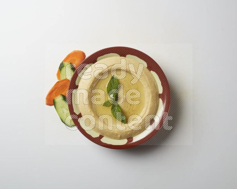 Hummus in a traditional plate garnished with mint on a white background