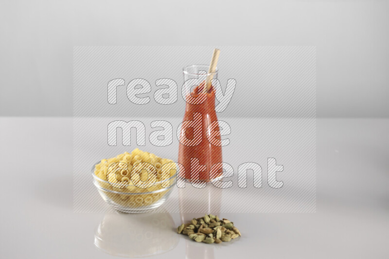 Raw pasta with tomatoe pasta with different ingredients such as cherry tomatoes, basil, garlic, bay laurel, cardamom, white pepper, black pepper, red chilis and wheat stalks on light grey background