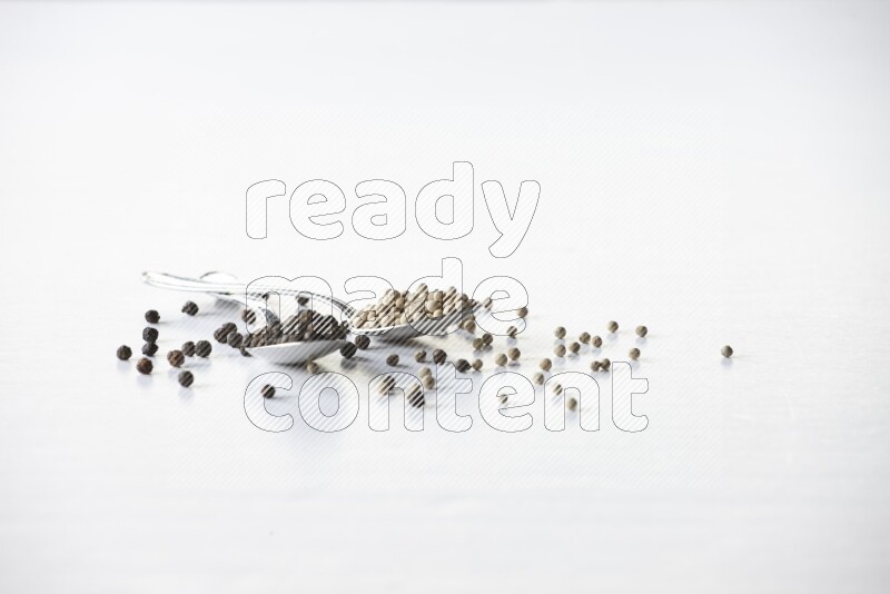 2 metal spoons full of black and white pepper beads with spreaded beads on white flooring