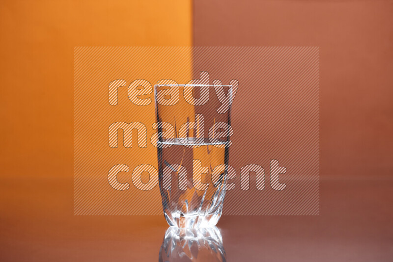 The image features a clear glassware filled with water, set against orange and dark orange background