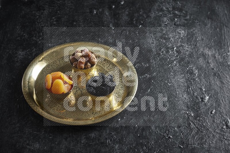 Dried fruits in metal bowls on a tray in a dark setup