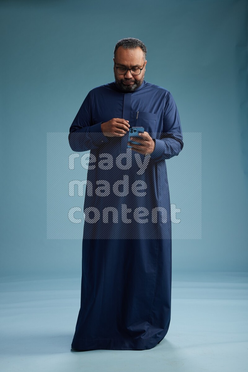 Saudi Man without shimag Standing texting on phone on blue background