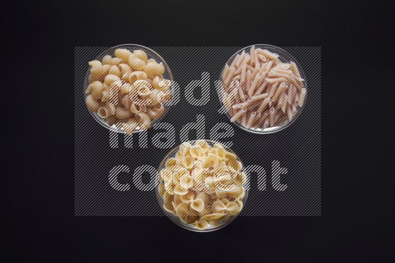 Different pasta types in glass bowls on black background