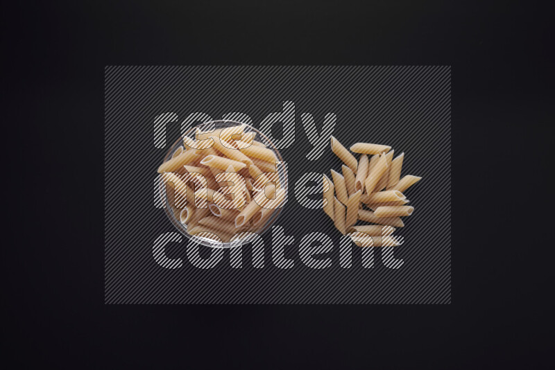 Penne pasta in a glass bowl on black background