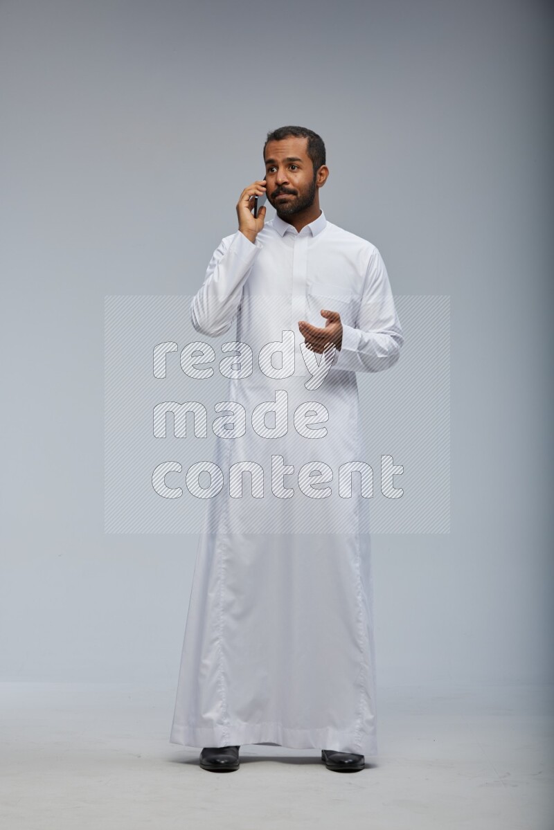 Saudi man wearing Thob standing talking on phone on Gray background