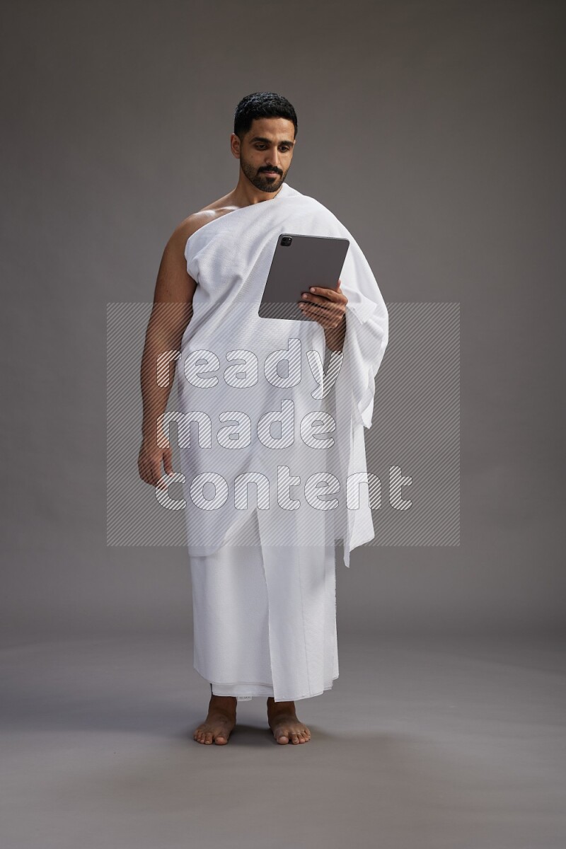 A man wearing Ehram and holding a tablet on gray background
