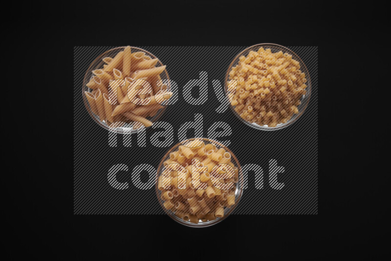 Different pasta types in glass bowls on black background