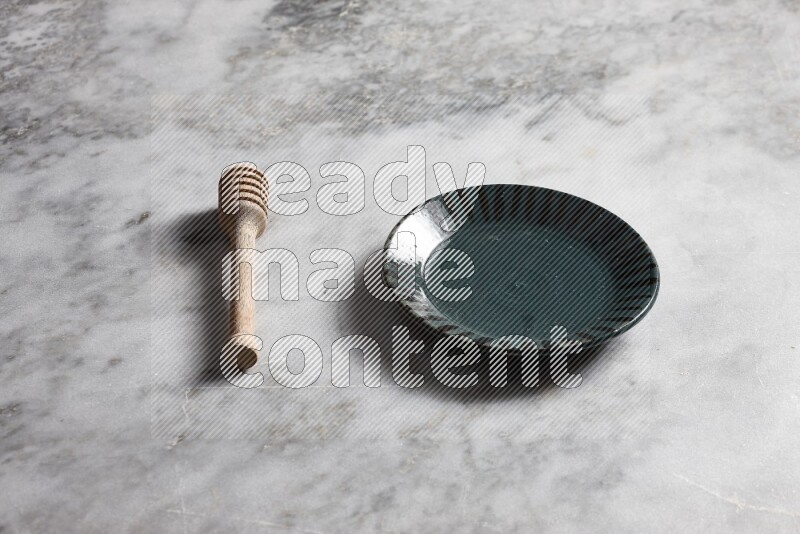 Multicolored pottery plate with wooden honey dipper on the side on grey marble background