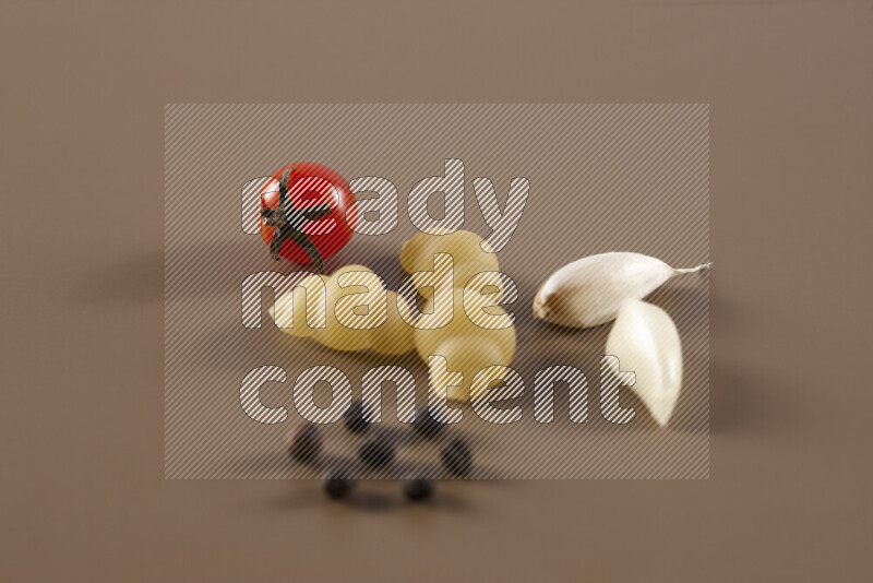 Raw pasta with different ingredients such as cherry tomatoes, garlic, onions, red chilis, black pepper, white pepper, bay laurel leaves, rosemary and cardamom on beige background
